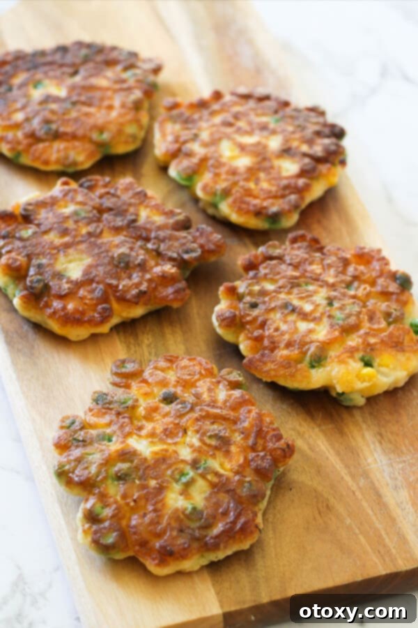Vibrant Pea and Sweet Corn Fritters 3 A close-up shot of golden-brown Pea & Sweet Corn Fritters arranged on a wooden board, showcasing their texture.