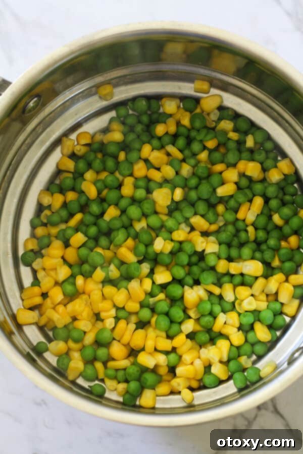 Vibrant Pea and Sweet Corn Fritters 4 Step-by-step image showing frozen peas and corn boiling in a small pot of water.