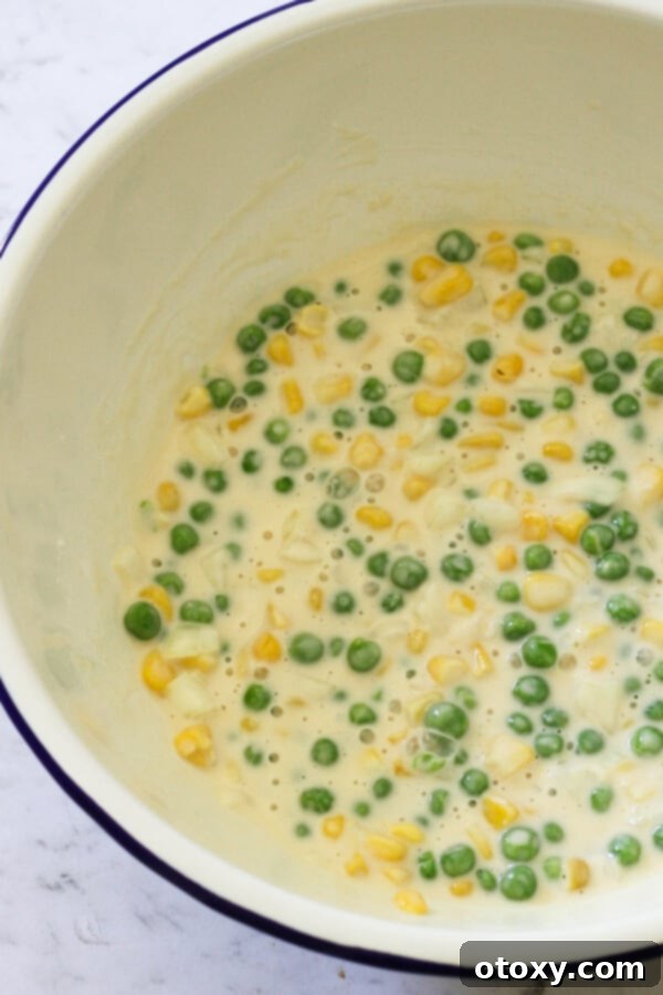 Vibrant Pea and Sweet Corn Fritters 5 Step-by-step image showing the fritter batter being mixed in a large bowl with peas, corn, and onion.