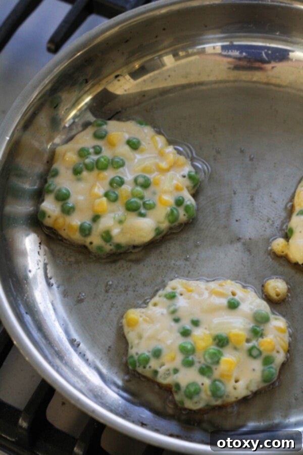 Vibrant Pea and Sweet Corn Fritters 6 Step-by-step image of Pea & Sweet Corn Fritters sizzling and cooking in a hot frying pan, turning golden brown.