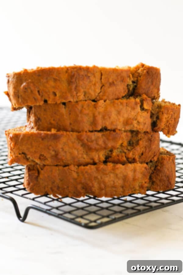Velvety Buttermilk Banana Bread 3 Several slices of golden-brown Buttermilk Banana Bread stacked on a metal wire cooling rack, showcasing its moist texture.