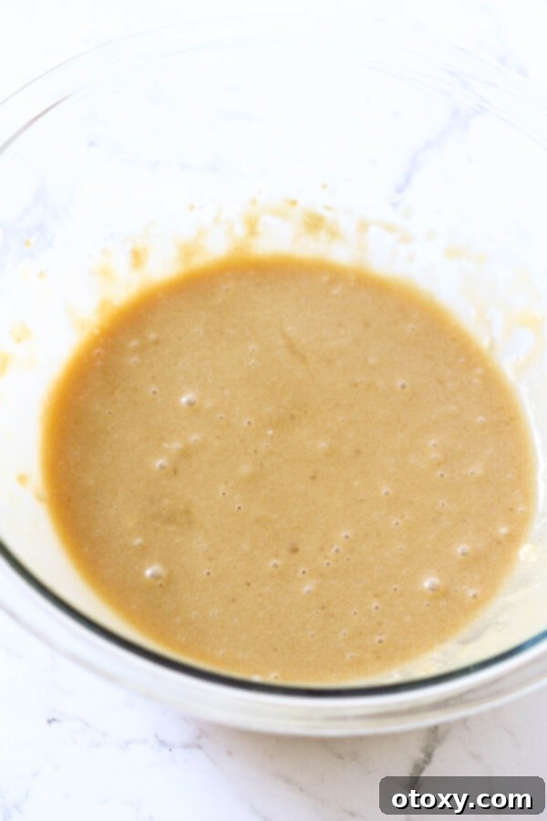 Velvety Buttermilk Banana Bread 6 Wet ingredients for banana bread, including mashed roasted bananas, mixed together in a large glass bowl, ready for dry ingredients.