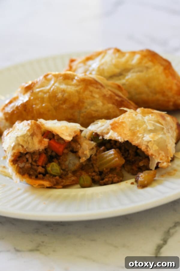 Freshly baked beef pasties on a clean white plate, highlighting their golden-brown crust.
