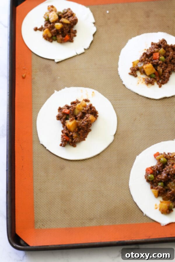 Puff pastry rounds arranged on a baking tray, each with a spoonful of savoury mince filling in the middle.