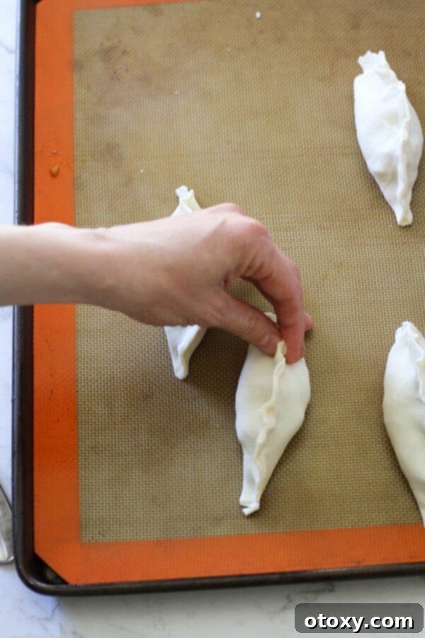 A hand carefully crimping the edges of a beef pasty with fingers to seal the filling.