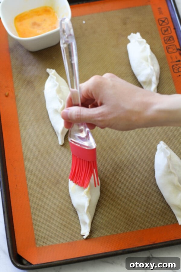 Several beef pasties, freshly shaped and egg-washed, arranged on a baking tray and ready for the oven.