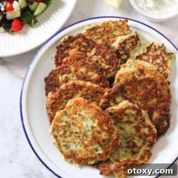 Crispy and golden Kolokithokeftedes, Greek Zucchini Fritters, garnished with fresh herbs and served with a creamy dip.
