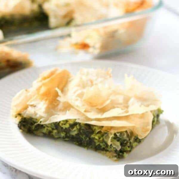 A golden-brown, flaky slice of Spanakopita, traditional Greek Spinach Pie, revealing a savory filling of spinach and cheese.