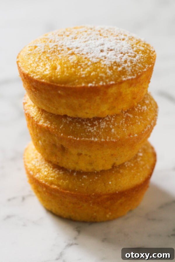 Zesty Orange Almond Tea Cakes 10 Orange and almond cakes cooling on a wire rack, next to fresh oranges.