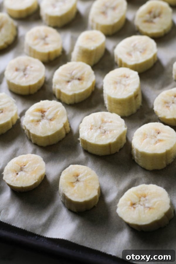 Perfectly arranged banana slices on a baking tray lined with parchment paper, prepared for the flash-freezing process.