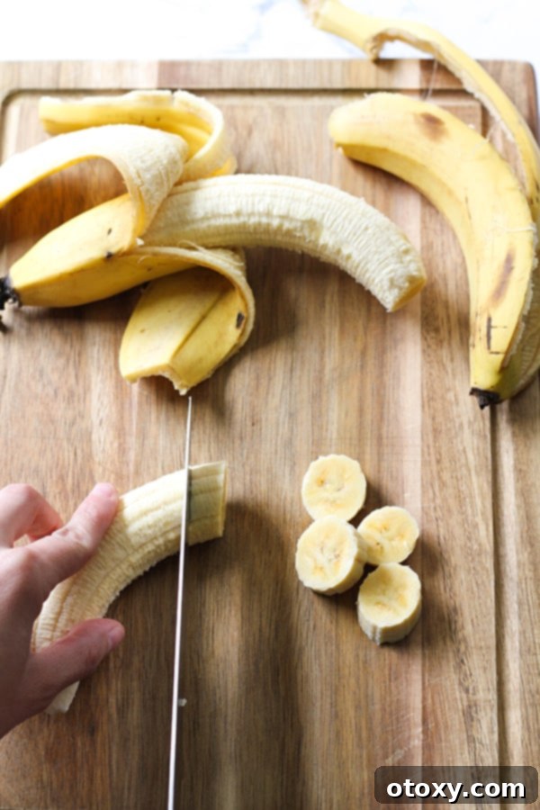 A hand expertly slicing a ripe banana into uniform rounds on a rustic wooden cutting board, preparing them for freezing.