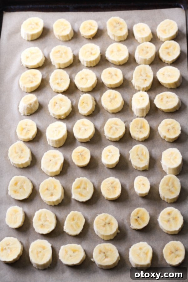 Multiple banana slices meticulously arranged in a single layer on a parchment-lined baking tray, ready to be flash-frozen individually.