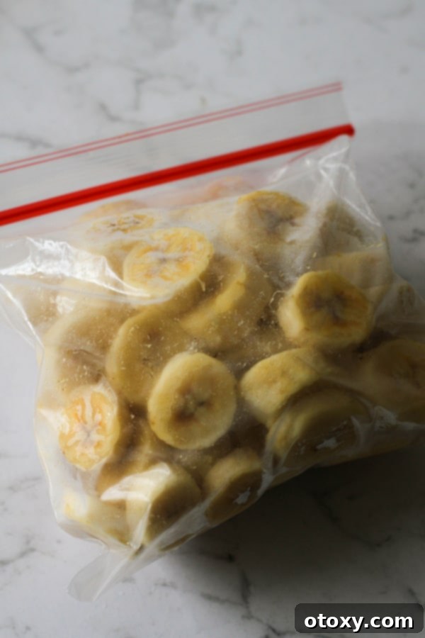 A hand gently dropping individually flash-frozen banana slices into a freezer-safe ziplock bag for efficient and long-term storage.