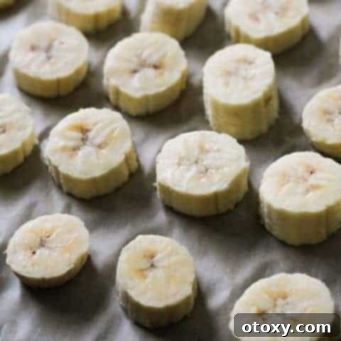 Perfectly arranged banana slices on a baking tray, ready for freezing, as part of the recipe guide.