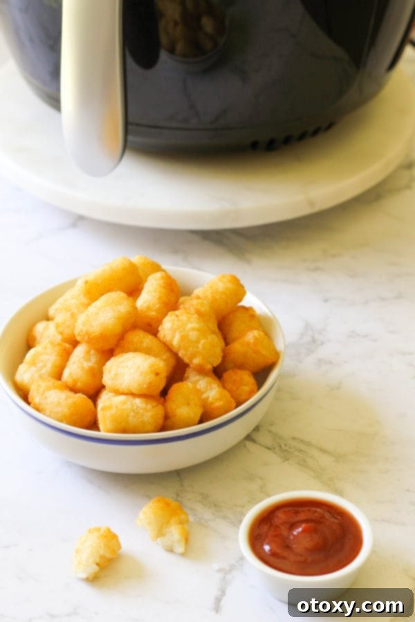 Another view of a white serving bowl generously filled with perfectly golden and crispy air fryer tater tots.