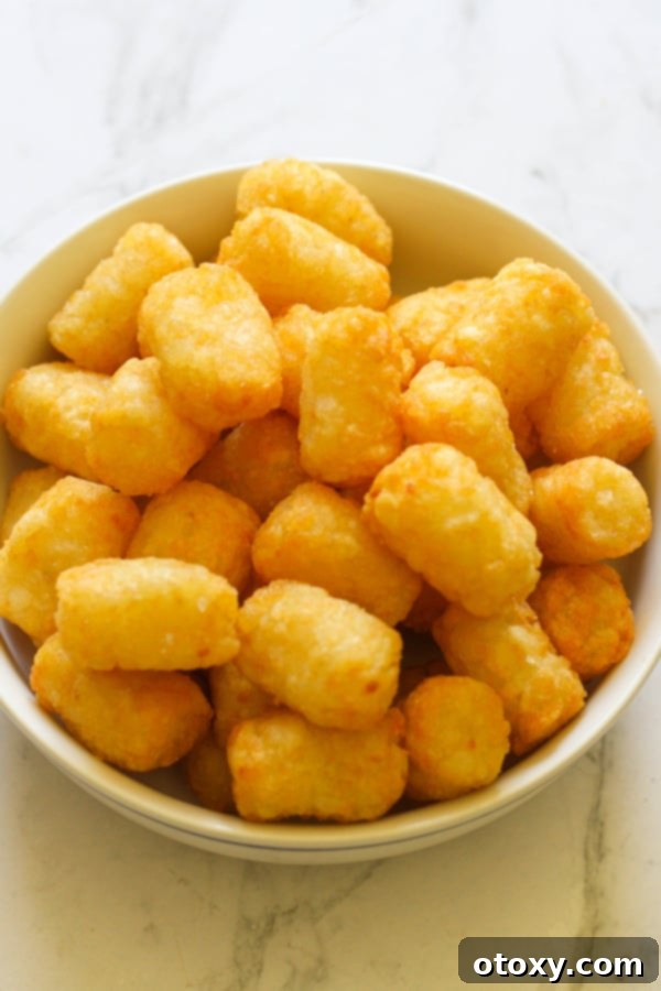 A close-up shot of crispy air fryer tater tots nestled together in a white bowl, highlighting their golden texture.