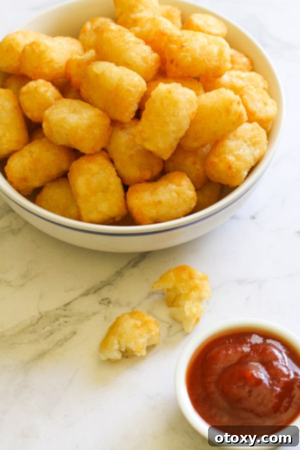 A pristine white bowl filled to the brim with perfectly cooked, golden-brown air-fried tater tots, ready for dipping.