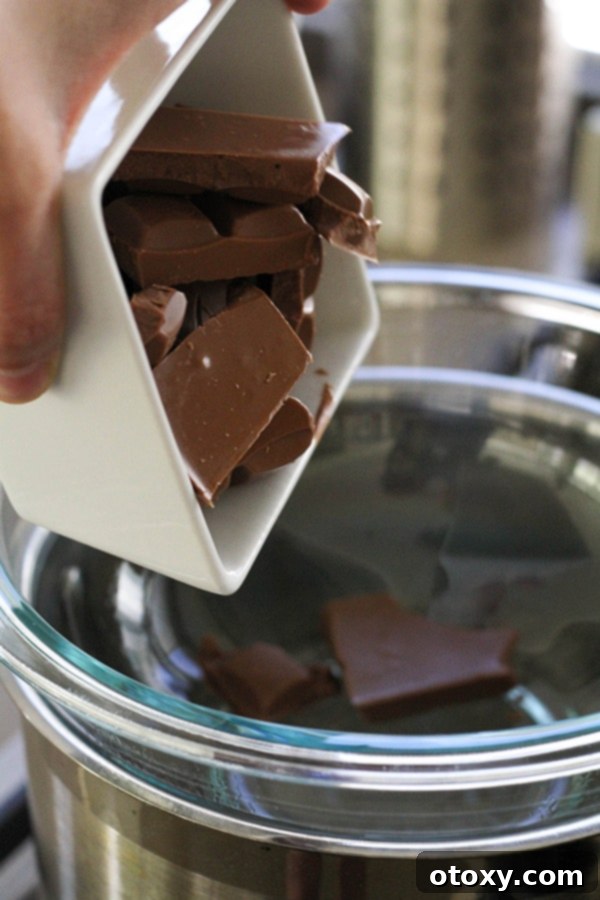 A hand pouring a bowl of chopped chocolate into a glass bowl over a saucepan.