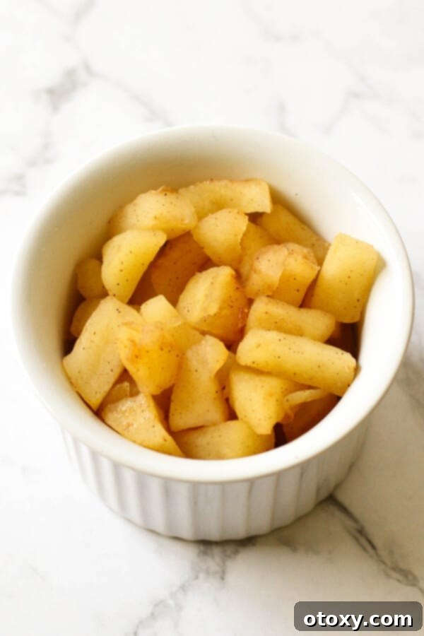 A white bowl filled with perfectly stewed cinnamon apple pieces, ready for use in delicious turnovers.