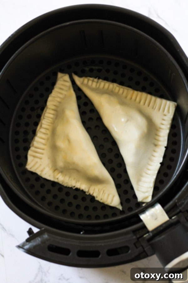 Two golden-brown apple turnovers, perfectly puffed and baked, nestled in an air fryer basket after cooking.