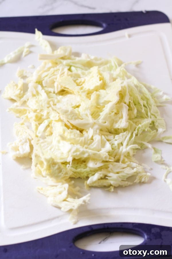 Crispy Pan-Fried Cabbage 3 Freshly shredded green cabbage spread out on a white cutting board, ready for cooking.
