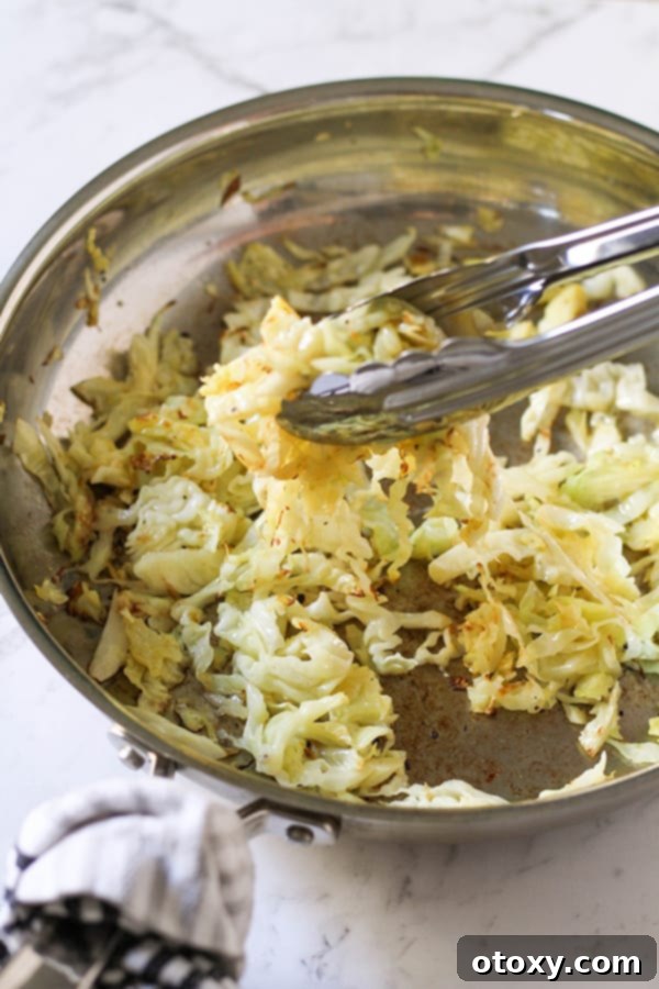 Crispy Pan-Fried Cabbage 4 Sautéed cabbage actively cooking and browning in a stainless steel frying pan.