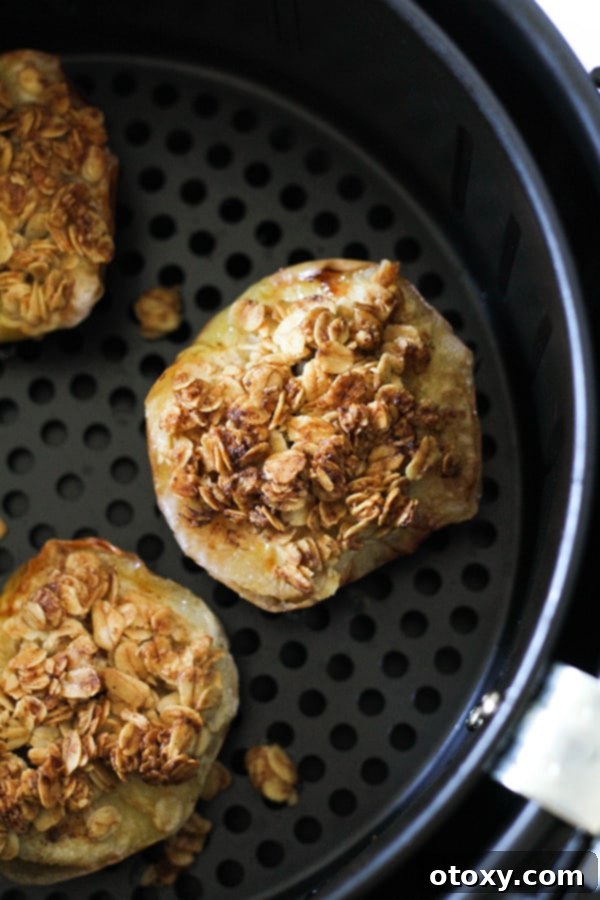 Cooked baked apples nestled perfectly within an air fryer basket, showcasing their golden-brown topping.