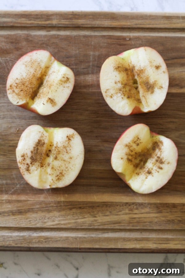 Apple halves, cored and generously covered with cinnamon on a wooden board, ready for the next step.