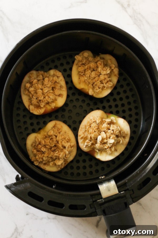 Apple halves generously topped with a mixture of oats and spices, nestled in an air fryer basket, ready to cook.