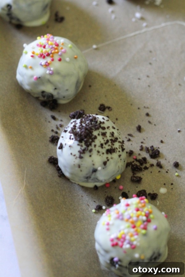 Creamy Oreo Cheesecake Truffles 9 oreo balls laying on baking tray covered in cookie crumbs and sprinkles.