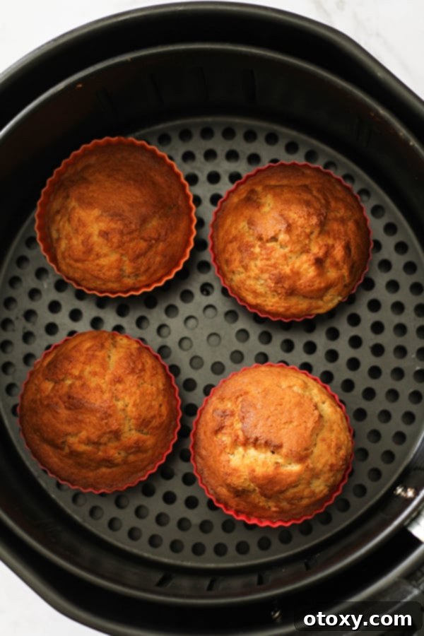 Air fryer basket filled with beautifully baked banana muffins in silicone cases, showing their golden tops.
