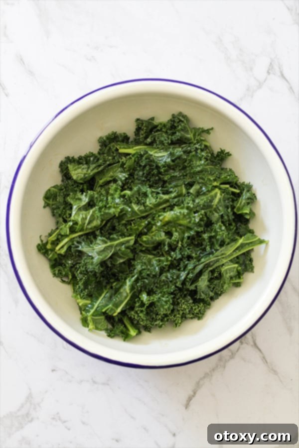 Sweet and Salty Air Fryer Kale Crisps 6 A vibrant green bowl filled with thoroughly massaged kale leaves, glistening with olive oil and maple syrup, ready for air frying.