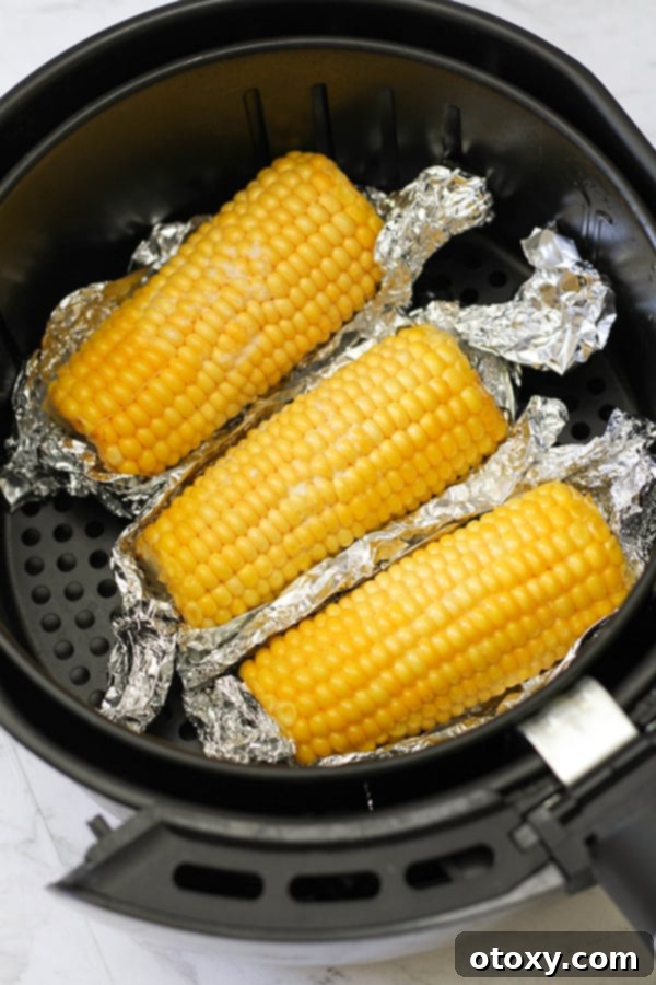 Ears of corn wrapped in foil nestled inside an air fryer basket, ready for cooking.