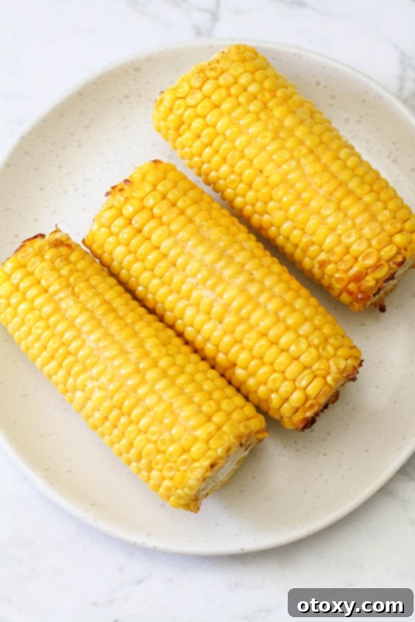 Freshly air-fried corn on the cob, glistening with butter, presented on a clean white plate.