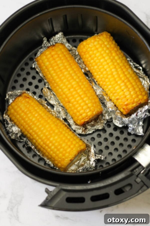 Cooked corn on the cob still in its foil, resting inside the air fryer basket before serving.