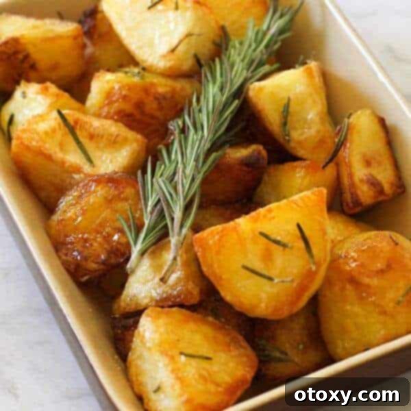 Crispy roast potatoes with rosemary sprigs, perfectly golden and seasoned, served in a white bowl.