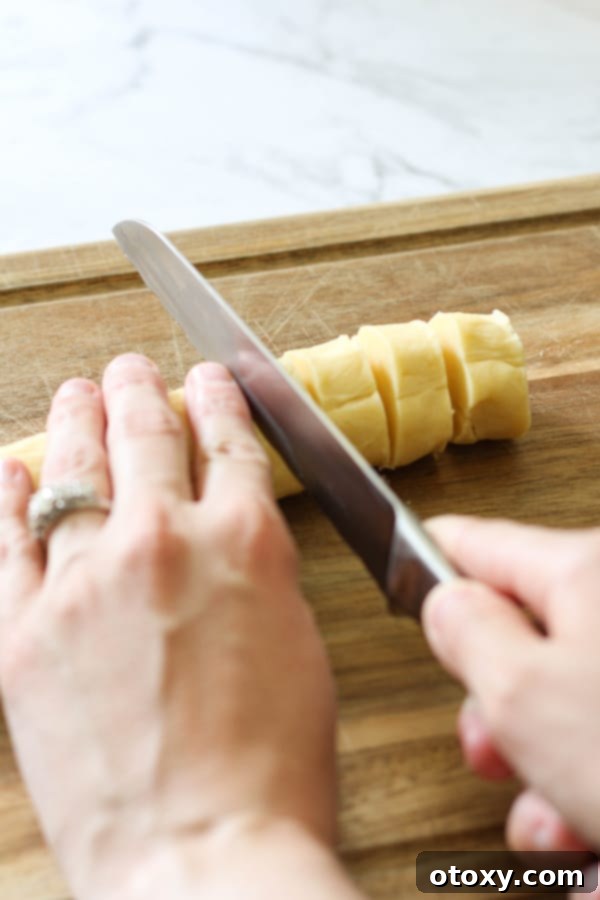 A hand slicing a chilled shortbread dough log into round cookies.