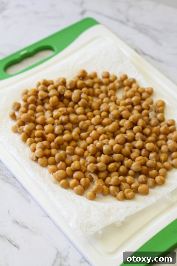 Drained and rinsed chickpeas spread on paper towels, being patted dry to remove moisture.