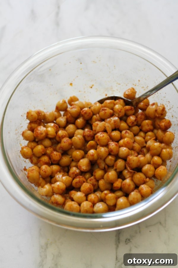 Chickpeas in a glass bowl, coated evenly with olive oil and a vibrant blend of spices.