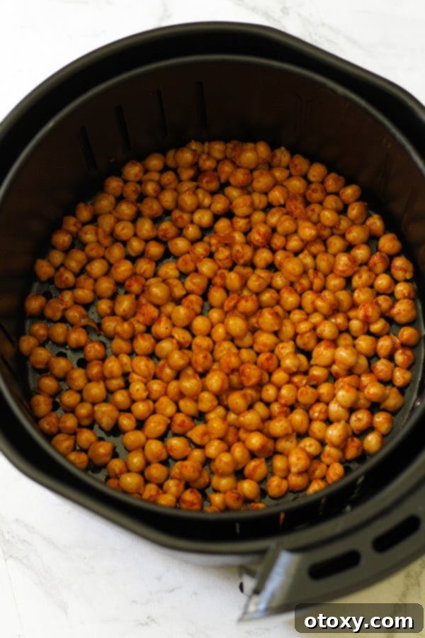 Seasoned chickpeas spread in a single layer inside an air fryer basket, mid-cooking process.