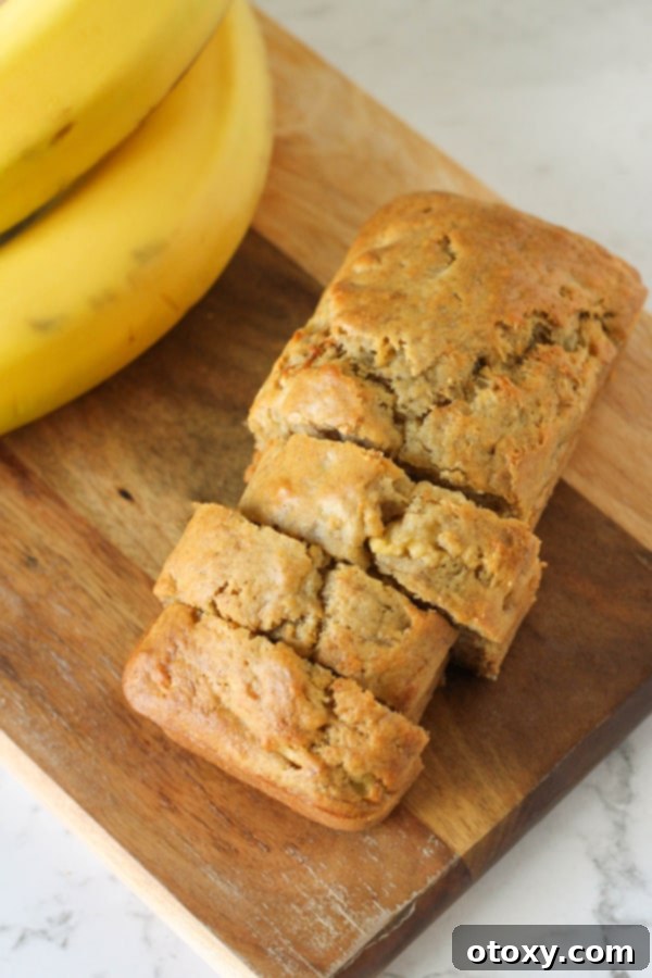 A single mini banana loaf, beautifully sliced to reveal its moist interior, resting on a wooden cutting board.