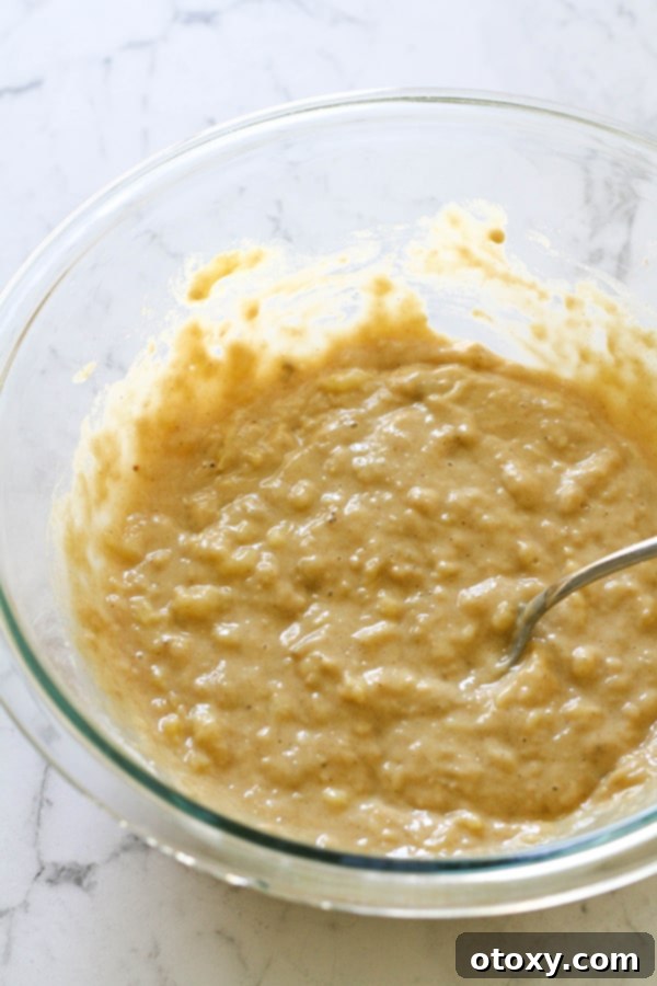 Thick, rich banana bread mixture in a large glass mixing bowl, showcasing its readiness for baking.
