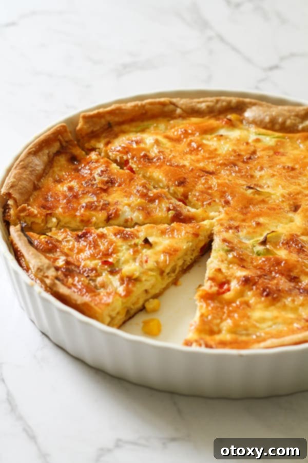 Fresh Garden Quiche 12 A vibrant slice of vegetarian quiche in a white quiche dish, showcasing its layers and golden crust.