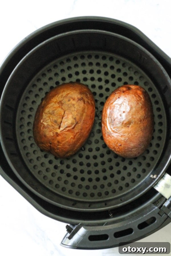 Air Fryer Potato Perfection 5 baked potatoes in an air fryer basket.