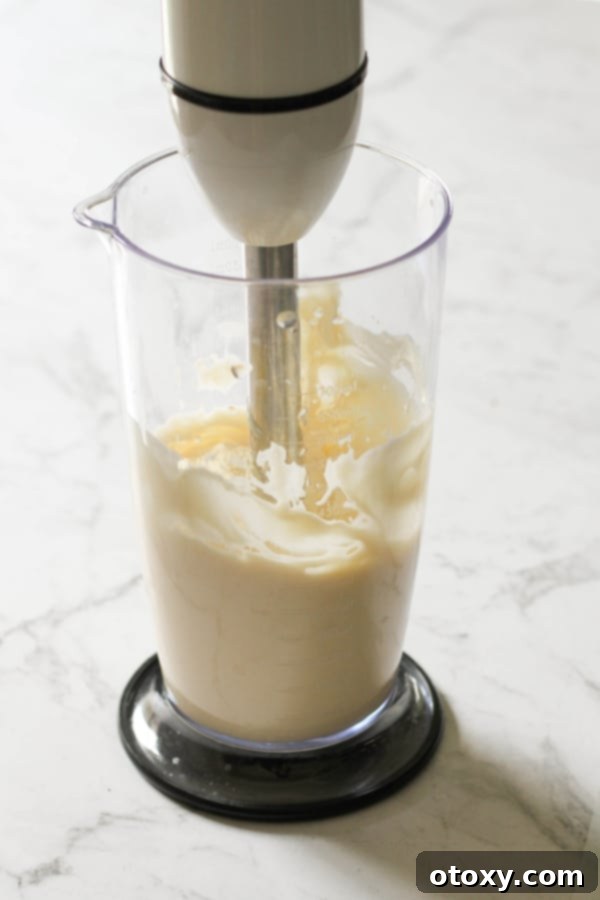 Mayonnaise being perfectly emulsified in a jar using an immersion blender, showing the creamy texture forming.