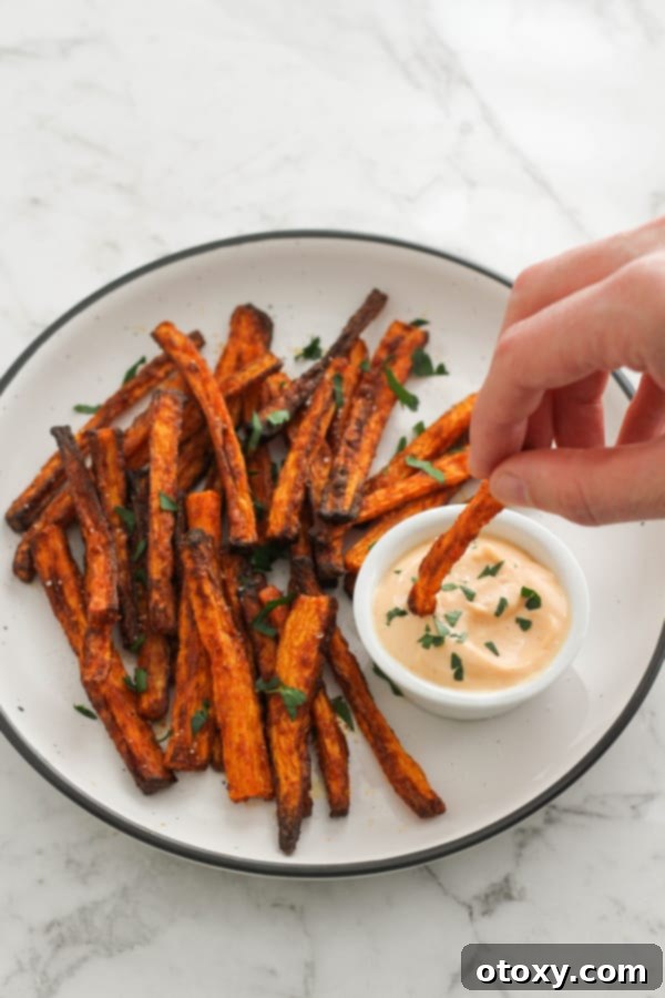 A hand dipping an Air Fryer Carrot Fry into a bowl of spicy mayonnaise.