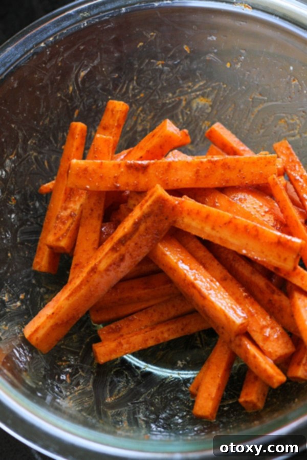Close-up of carrot fries evenly coated with seasonings in a glass bowl.