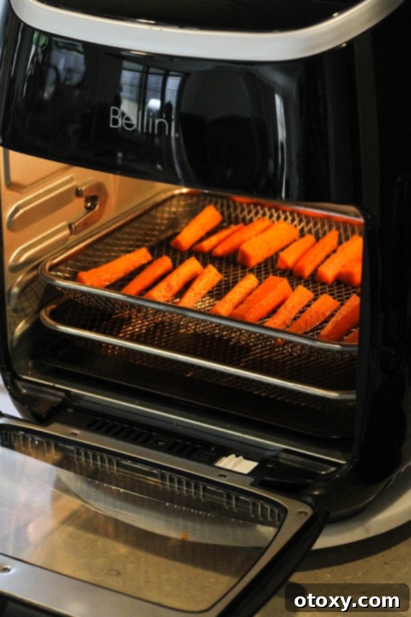 Carrot sticks cooking inside an air fryer basket, showing browning.