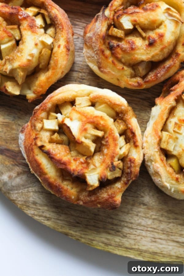 Air Fryer No Rise Apple Cinnamon Rolls 2 Golden brown Air Fryer Apple Cinnamon Rolls dusted with cinnamon on a rustic wooden cutting board, ready to be served.