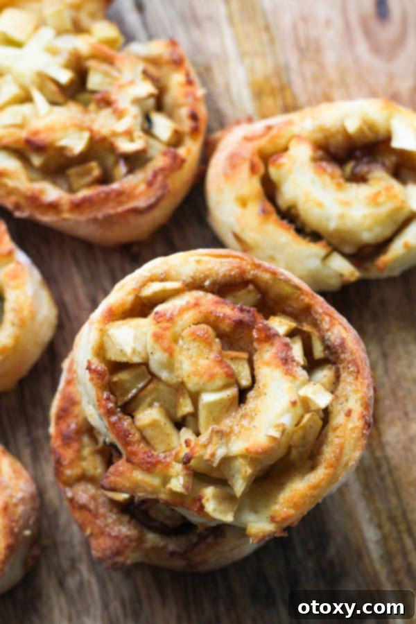 Air Fryer No Rise Apple Cinnamon Rolls 3 A closer look at Air Fryer Apple Cinnamon Rolls with their golden crust and visible apple filling, presented on a wooden board.